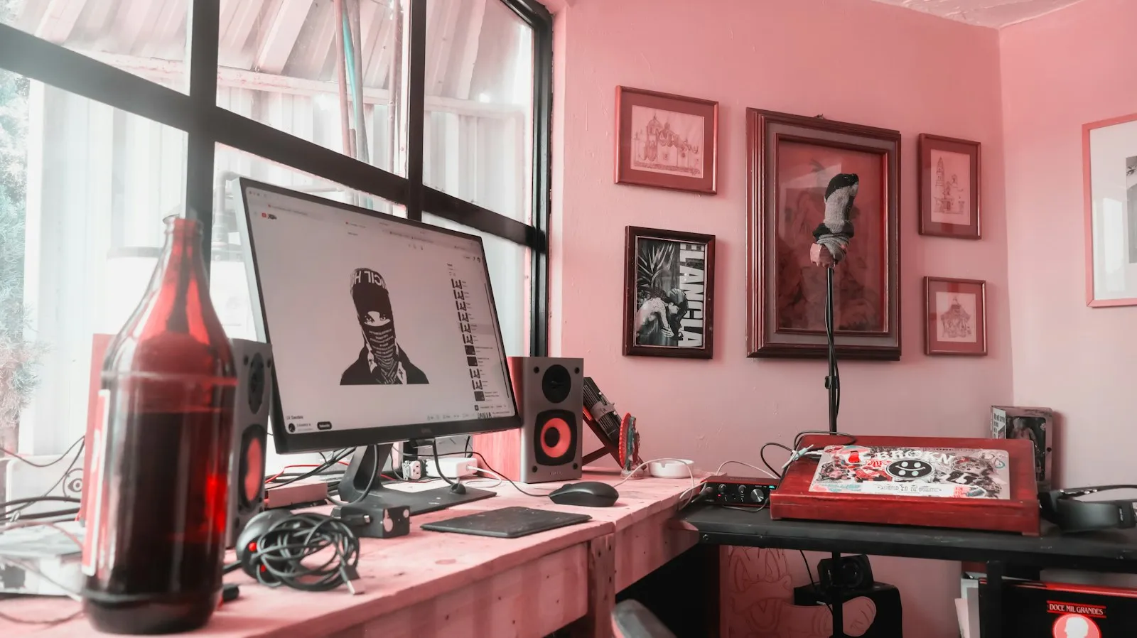 A home studio desk with speakers, a microphone and framed art