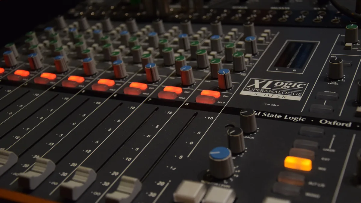 An analogue mixing desk in a recording studio, faders and channel strips in focus